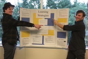 Two students point to different aspects of a presentation board 