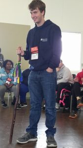 Matthias standing in the middle of a circle of students holding the spirit stick