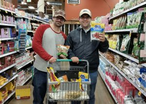 Two OLS students pose in an aisle of Fred Meyer showing the ingredients they've gathered in their shopping cart.
