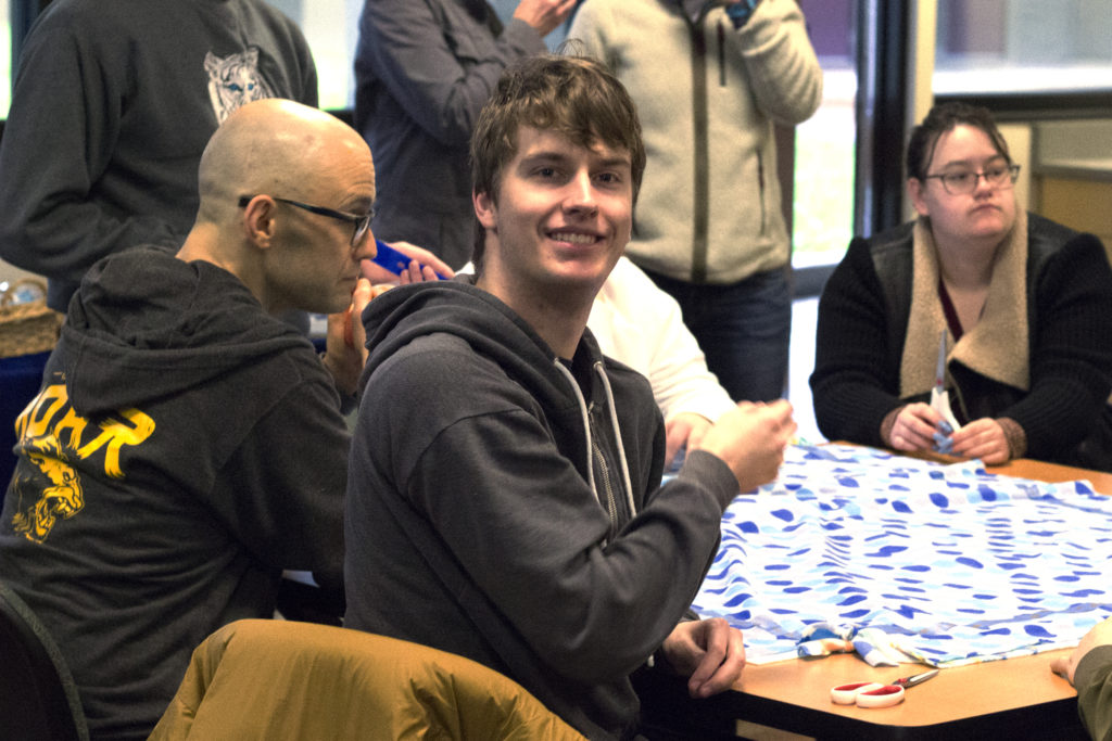 Student sitting at a table making blankets smiles for camera