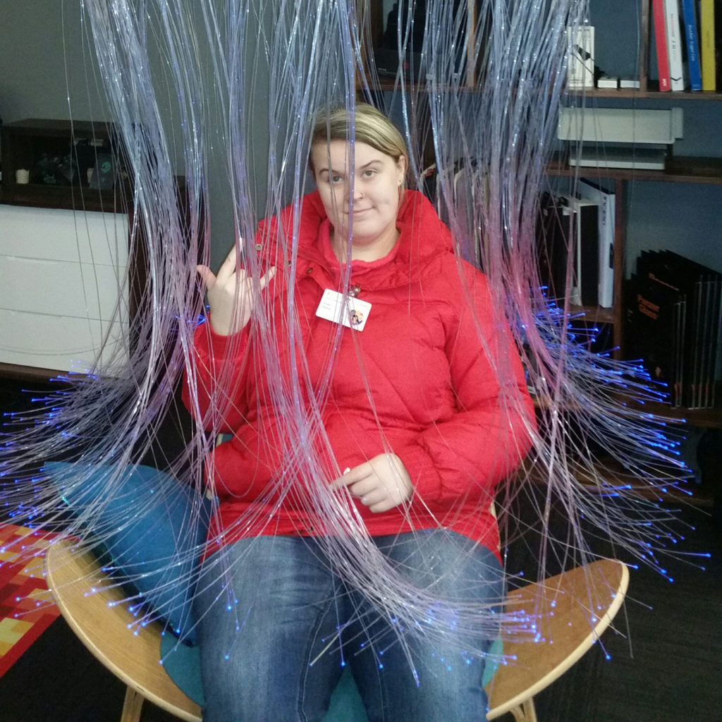 Student poses for a photo sitting under a funky jellyfish like chair