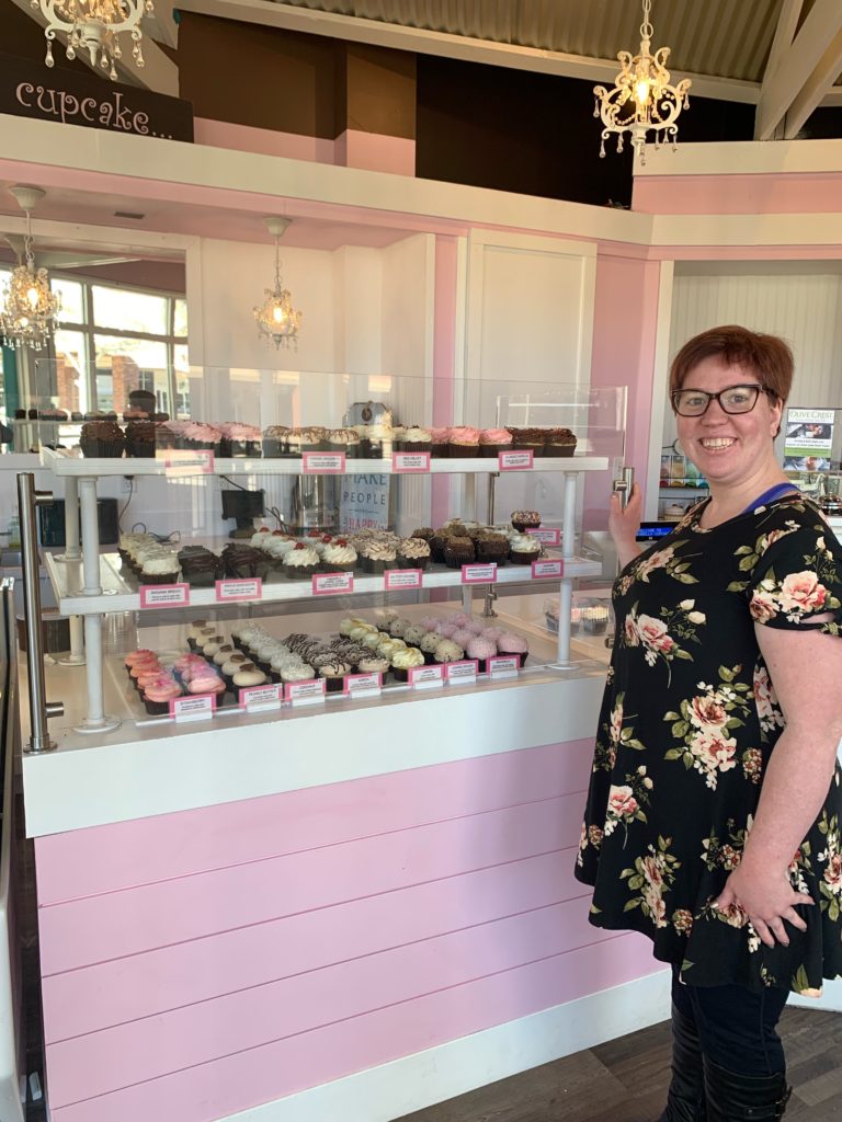 female stands in front of cupcake display at cafe