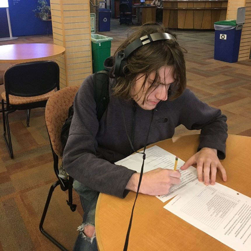 male student sits at table working on paperwork