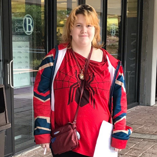 female student in bright Spiderman shirt poses in front of campus building