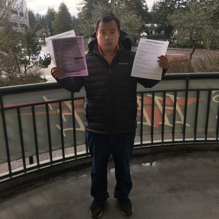 male student stands on balcony with paperwork