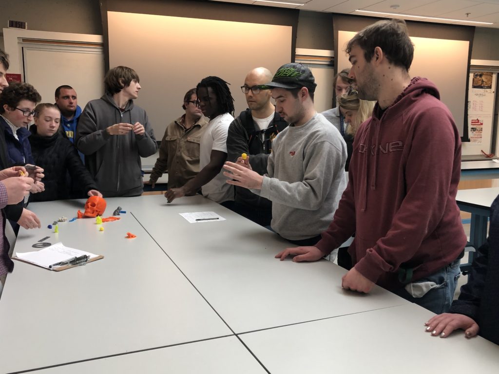 A small group of students stand at a table and check out a project together 