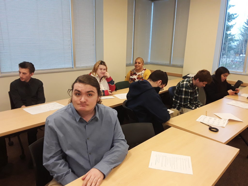 a group of young adults dressed for job interviews sit at desks