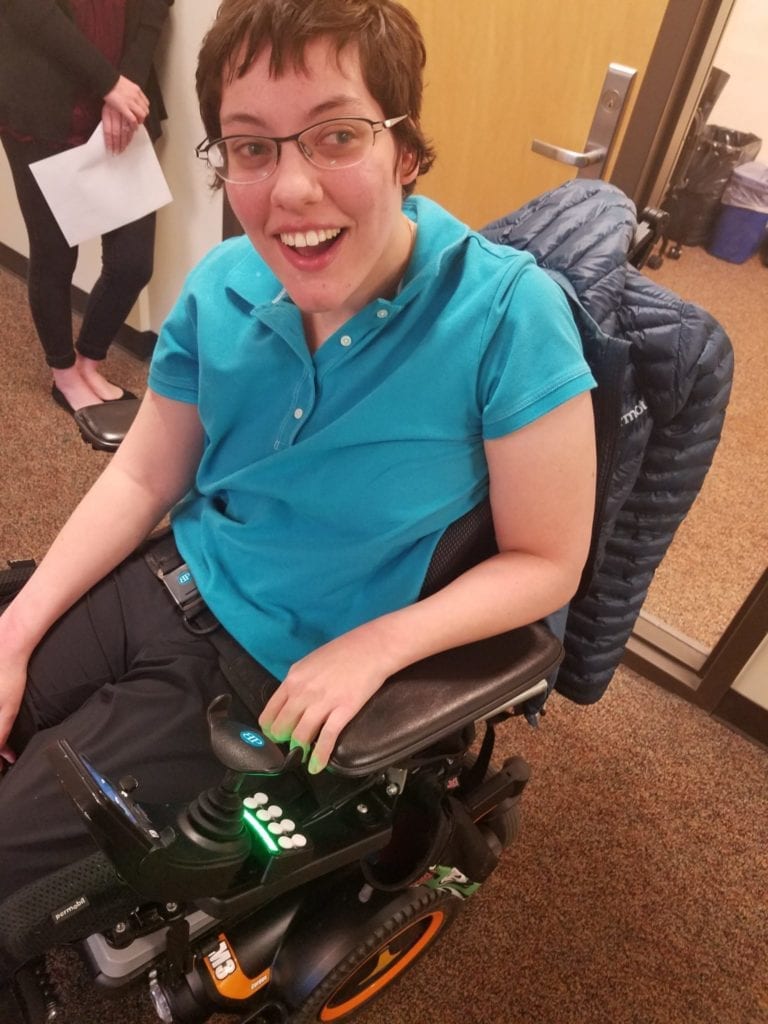 young adult woman in wheelchair waits outside a classroom