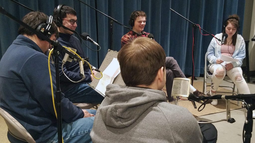 group of 5 students sit in a studio in front of microphones