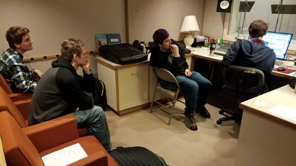 Three students watch an audio engineer make changes at a computer