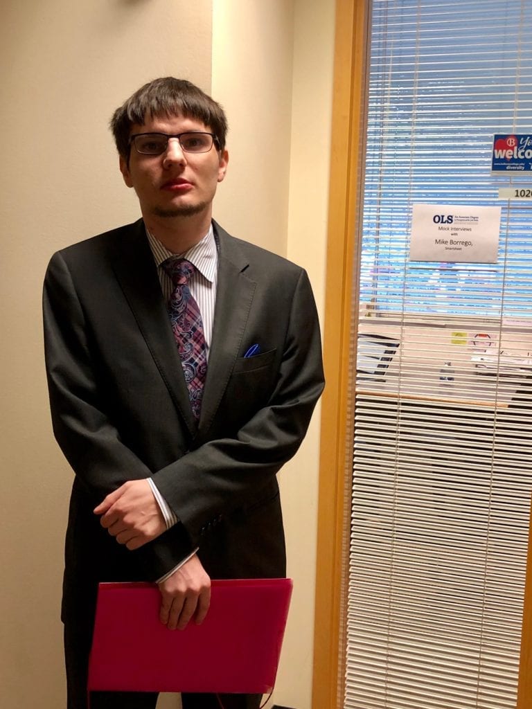 Young man dressed in suit and tie stands in front of professional office building waiting for job interview