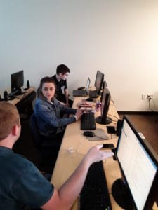 three young adult students work on a project on a computer