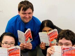 four students peek out from behind books they are reading