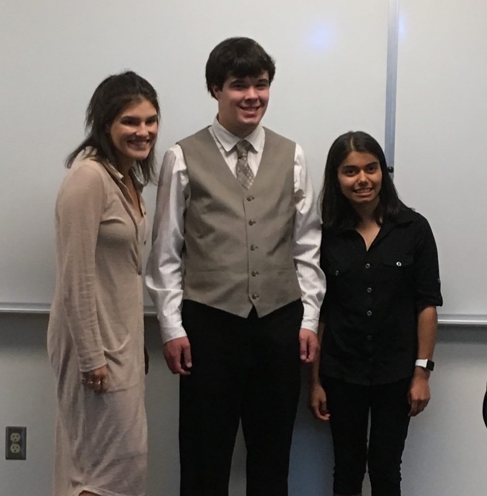 three young adults stand at the front of a college classroom