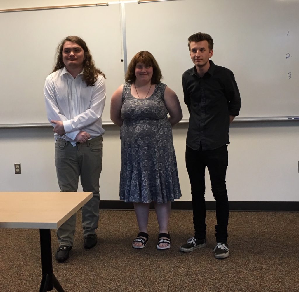 three young adults stand at the front of a college classroom