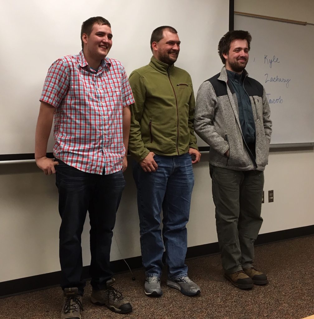 three young adults stand at the front of a college classroom