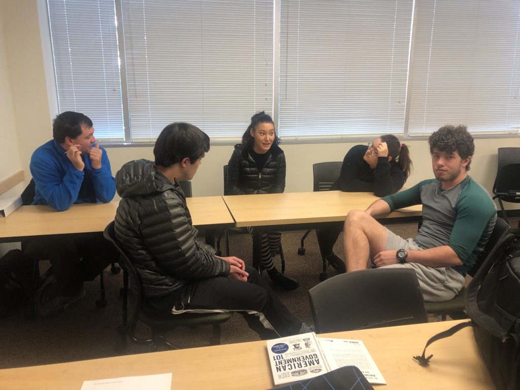 a group of 5 male and female students discuss politics around a table 