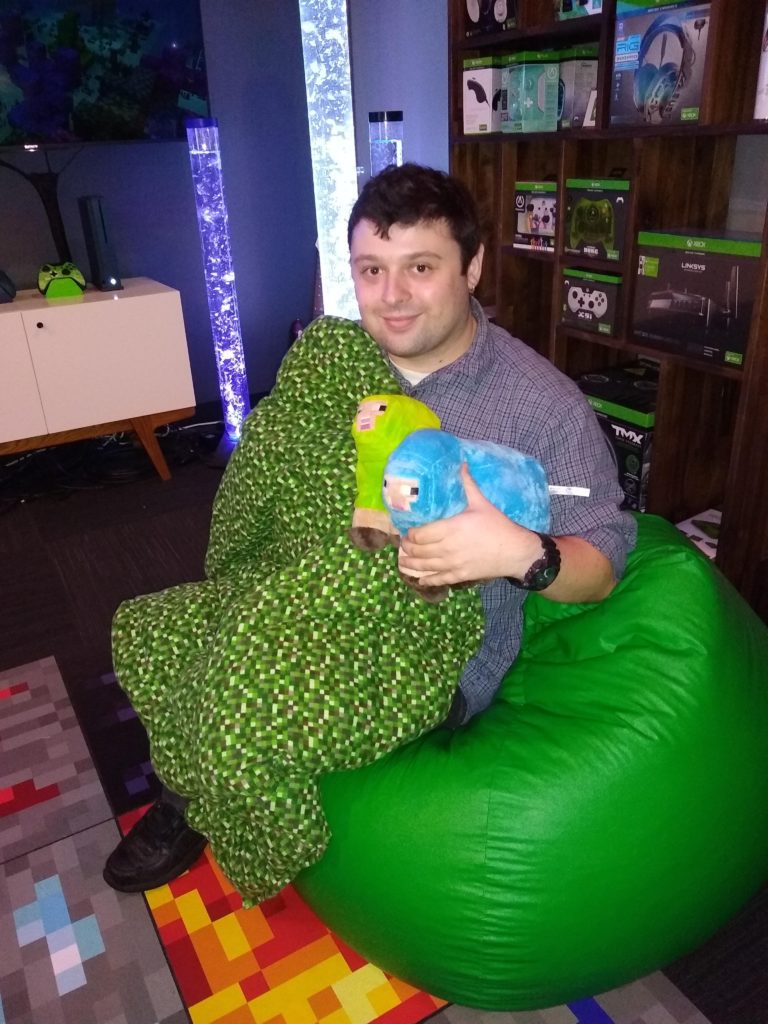 young adult man sits under a blanket with two techie stuffed animals