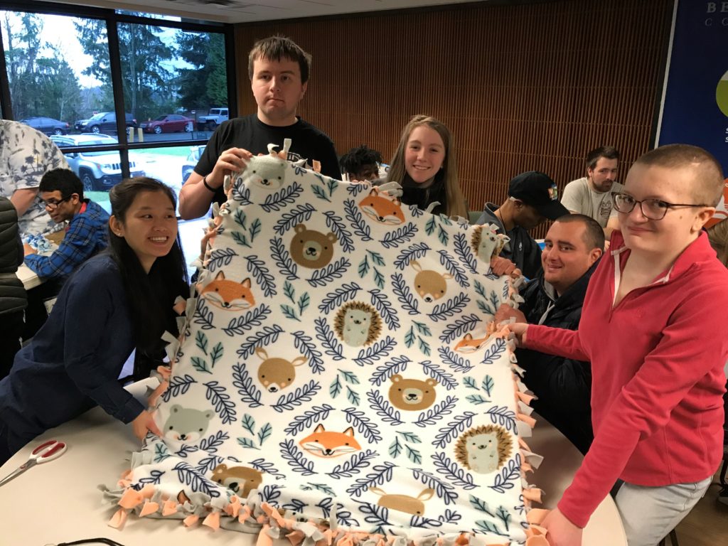 five young adults proudly hold up a fleece blanket