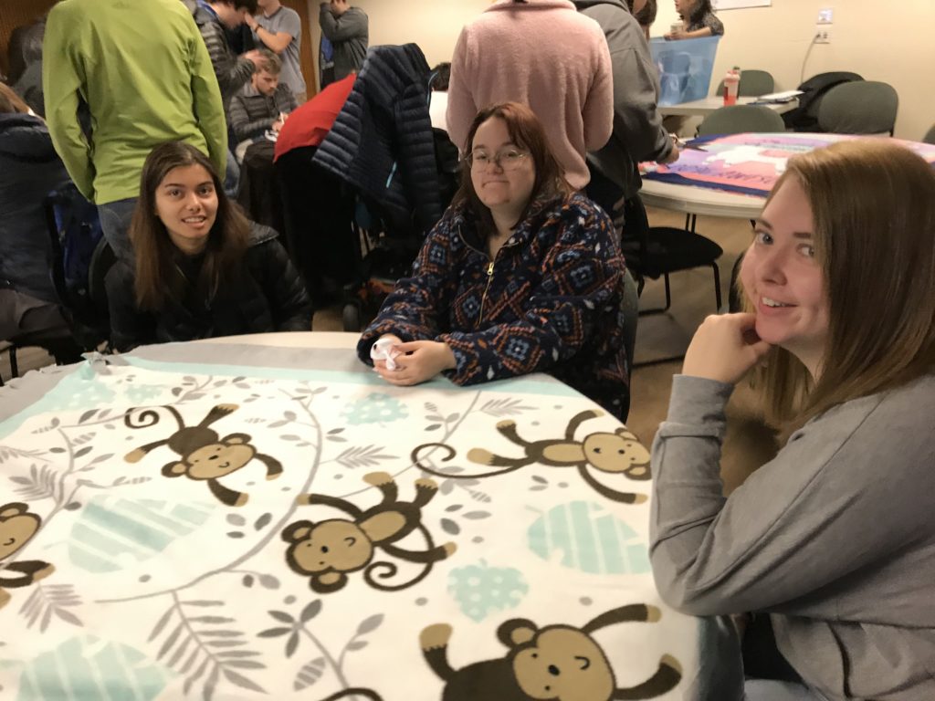 three young adults maken a fleece blanket