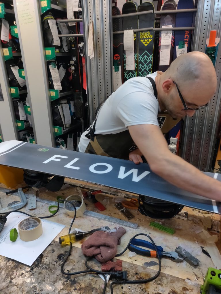 young man works on a snowboard in a shop