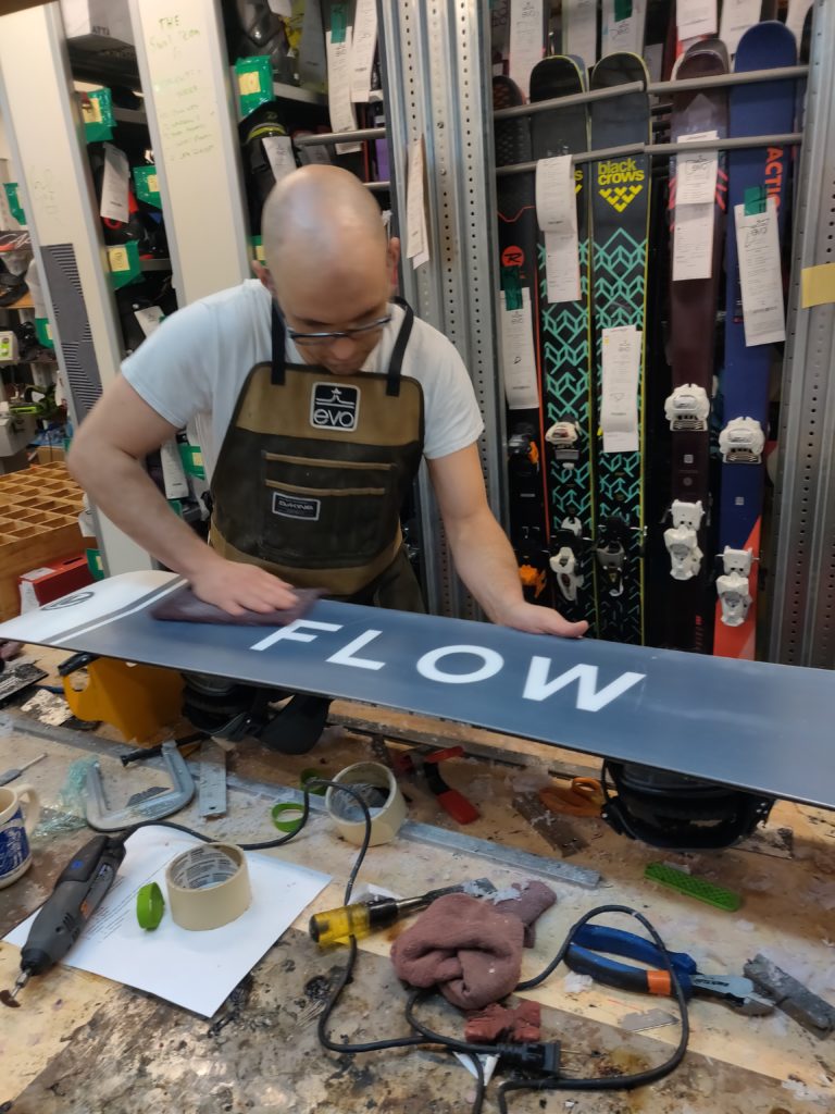 young man works on a snowboard in a shop