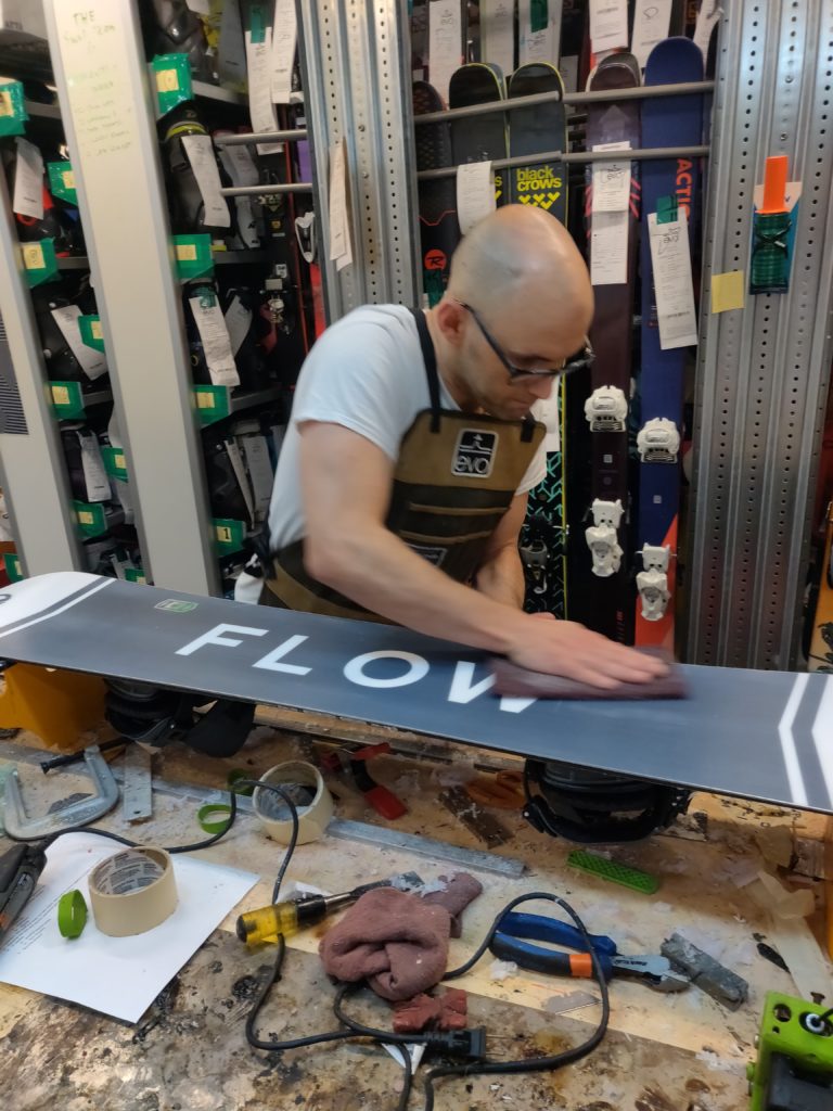 young man works on a snowboard in a shop