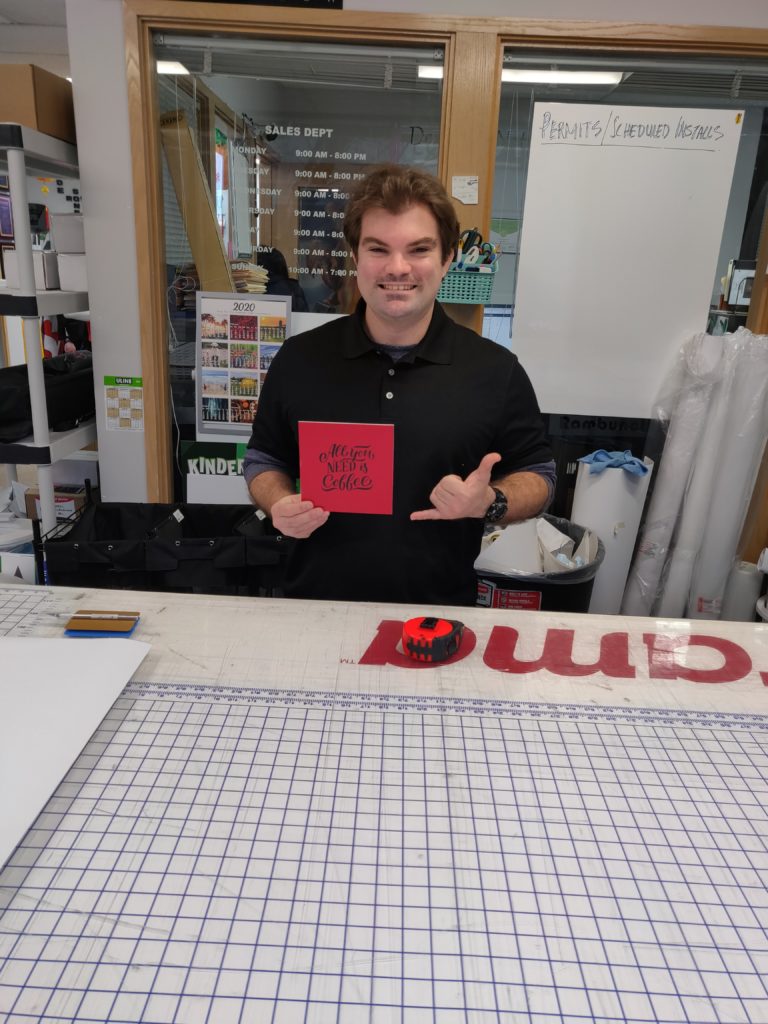 young adult man holds up graphic sign at print shop