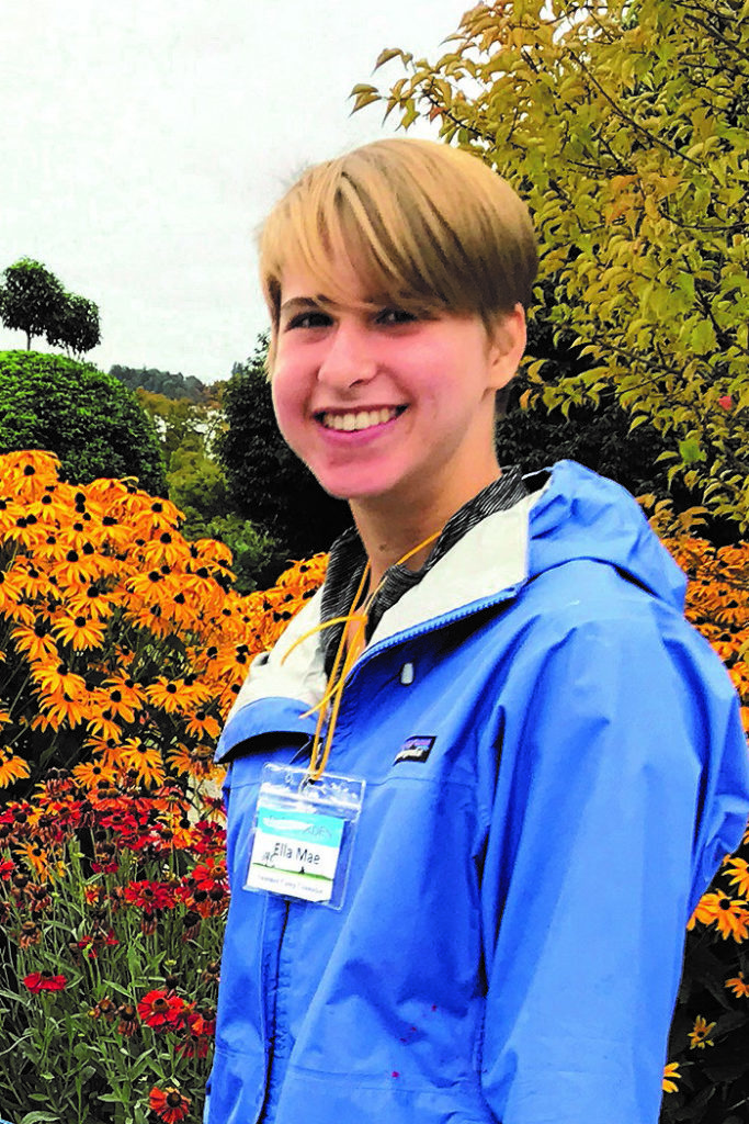 young woman in blue coat in front of flowers and foliage