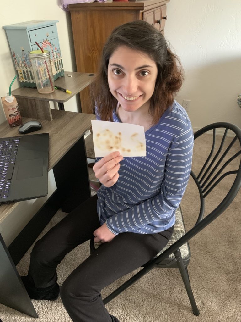 young lady holds up picture of the letters OLS she drew with invisible ink