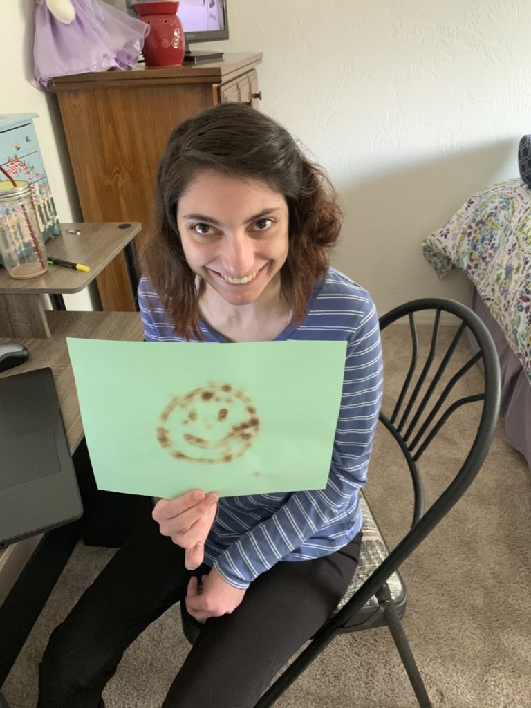 young lady holds up picture of a smiley face she drew with invisible ink