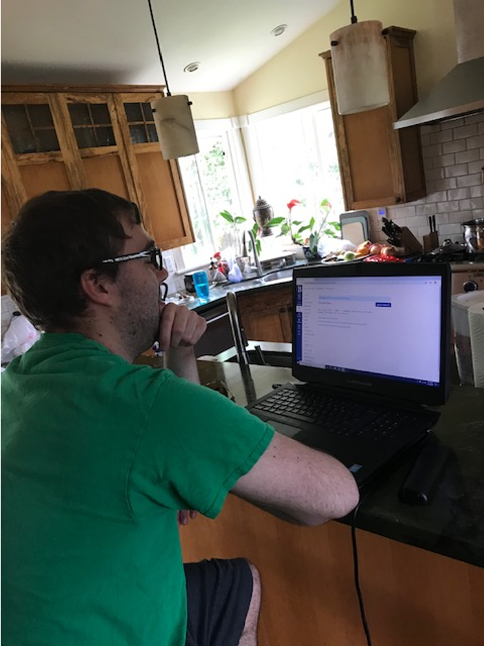 young adult man sits at kitchen counter working on laptop