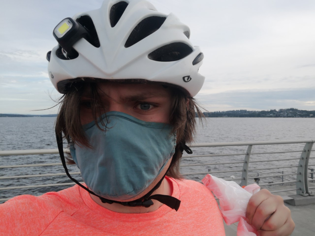 young man in face mask and bicycle helmet holds up garbage bag