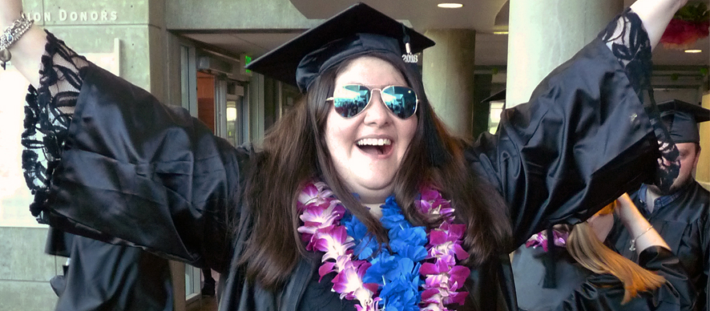 OLS student in camp and gown celebrates at graduation with a big smile and hands in the air