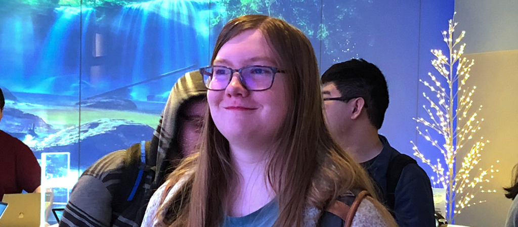 young woman with long hair and glasses looking off camera and smiling