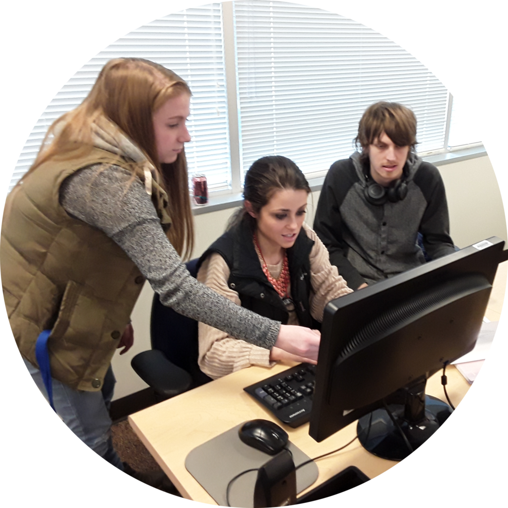 Three OLS students gathered around a computer doing group work in their OLS course