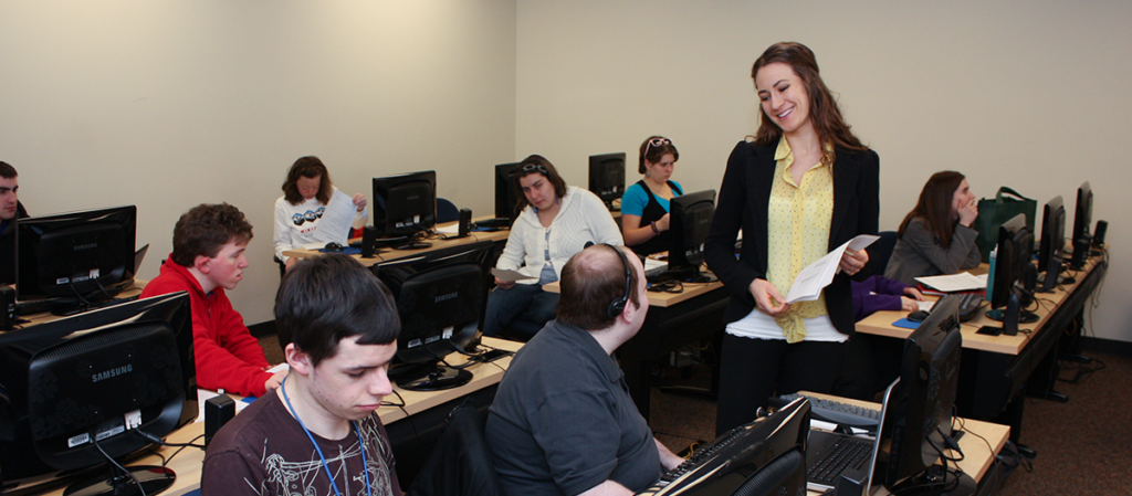 An OLS classroom with 8 students and an instructor talking to one student about their work