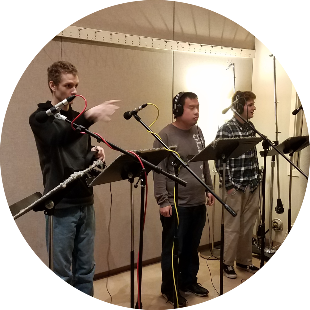 Three OLS students stand by microphones,  ready to record in a recording studio for the OLS Podcast Course.