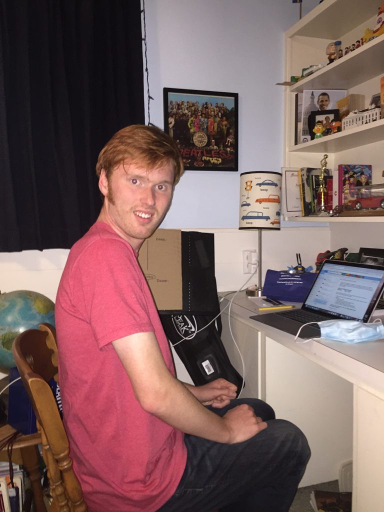 An OLS student smiles for a picture in front of him home desk