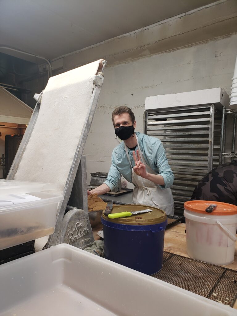 OLS student smiles from behind their mask and flashes the peace sign while working inside a bakery. 