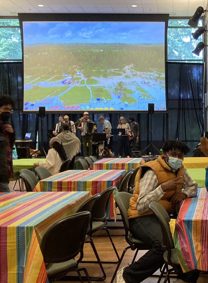 OLS Students in masks hanging out in the on campus cafeteria while a band plays music in the background.