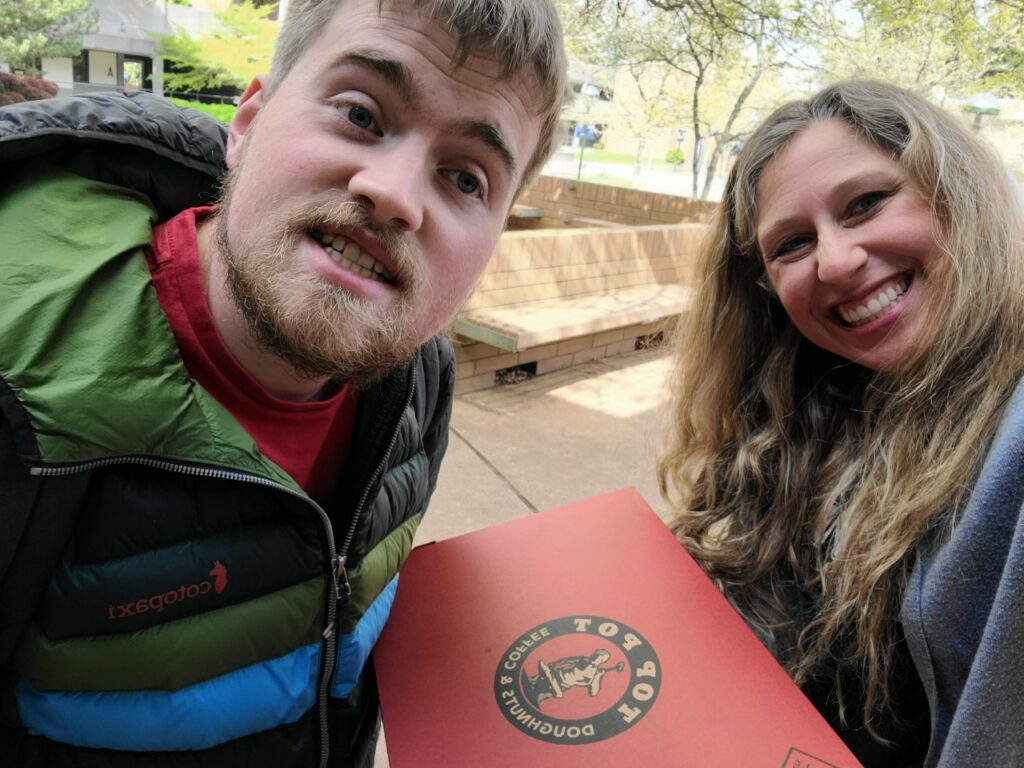 A young man and woman pose for a selfie photo outside with a box of donuts