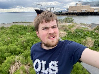 young man takes selfie of himself outside ona  sunny day with a bay in the background