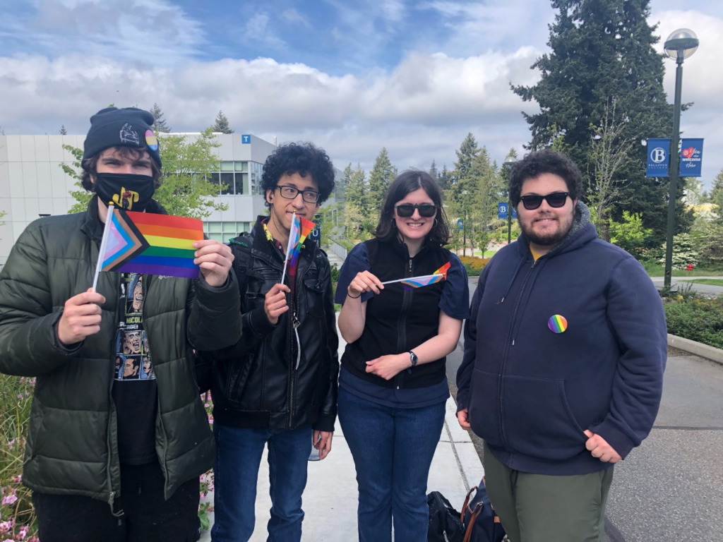 Four young college students outside with pride flag and pins