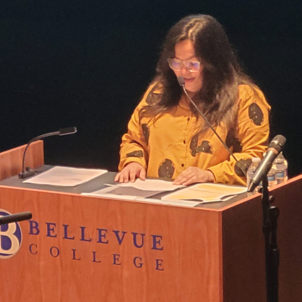 a woman in a yellow shirt stands behind a podium giving a speech