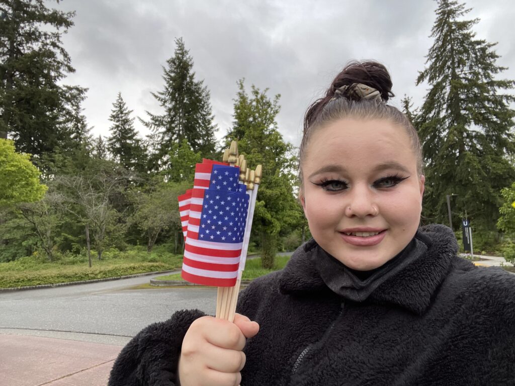 Selfie of an OLS student outside on campus holding a bunch of small US flag in her hand.  