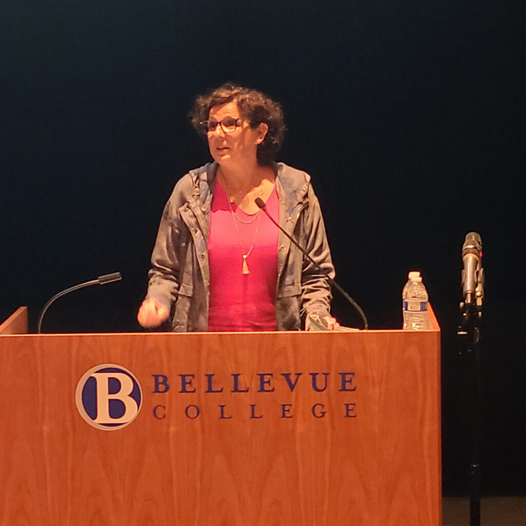 A woman in a pink shirt stand beind a podium on a stage