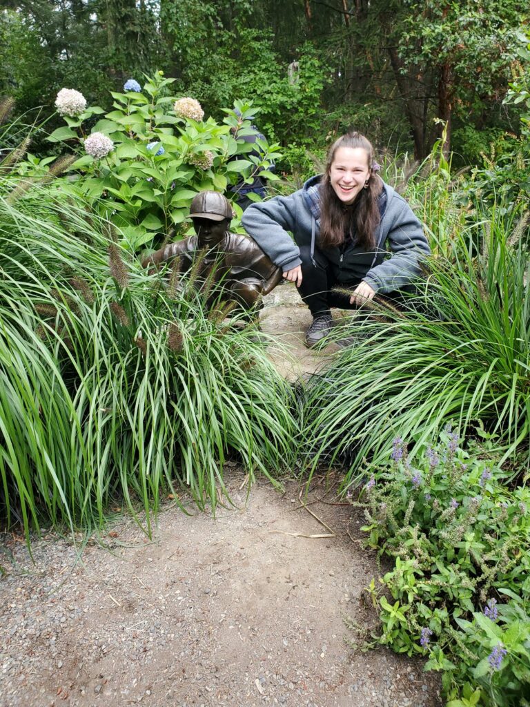 An OLS student crouches next to a statut on a trail at a park