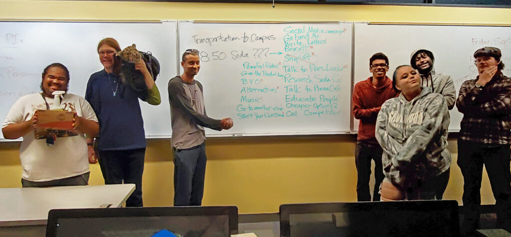 a group of seven OLS students pose in front of the whiteboard in class.