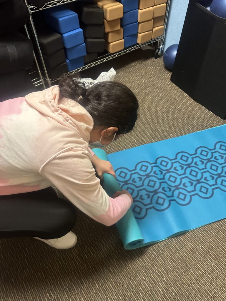 A young woman rolls up a yoga mat at her internship for OLS Bellevue College